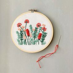 an embroidery project with red flowers and green leaves on the hoop next to a pair of scissors