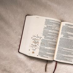 an open bible laying on top of a white blanket