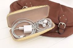 an open brown purse sitting on top of a white floor next to earbuds