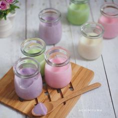 small jars filled with different colored liquids on a wooden tray next to flowers and spoons