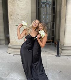 two beautiful young women standing next to each other in front of a building holding flowers