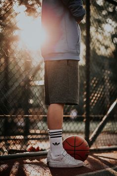 a man standing on top of a basketball court next to a fence with the sun behind him