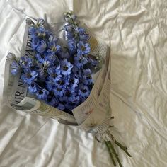 a bouquet of blue flowers sitting on top of a white sheet covered bed next to an open newspaper