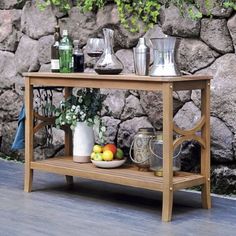 a wooden table with drinks and fruit on it in front of a stone wall, next to a potted plant