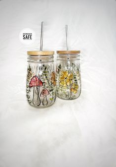 two glass jars with straws and flowers painted on them are sitting side by side