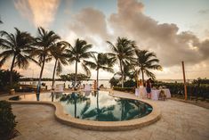 an outdoor pool surrounded by palm trees with people sitting at tables on the side and in the middle