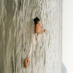 a woman in white shirt standing next to a wall with water coming out of it