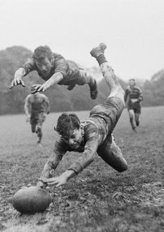 two men are diving for a ball in the mud while another man is running towards them