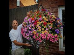 a man is holding a large hanging basket full of flowers