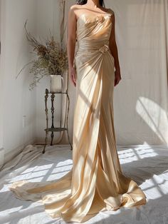 a woman in a long dress standing on a white floor next to a vase with flowers