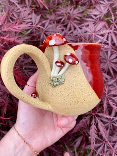 a hand holding a ceramic teapot with mushrooms on it and red leaves in the background