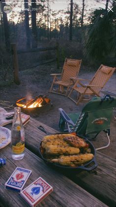 a table with food and drinks on it next to a fire pit in the woods