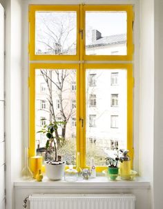 a window with yellow frames and potted plants in front of the window sill