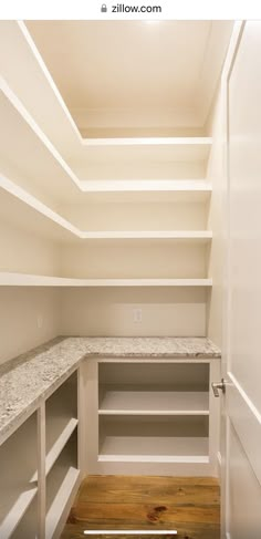 an empty walk in closet with white shelves and marble counter tops, along with wood flooring