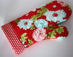 two oven mitts are sitting side by side on a white surface, one is red and the other has blue flowers