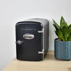 a black refrigerator sitting next to a potted plant on top of a wooden table