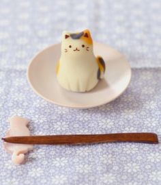 a small cat figurine sitting on top of a plate next to chopsticks