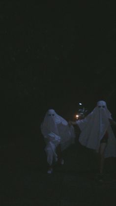 two people in ghost costumes walking through the dark