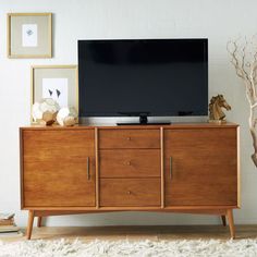 a flat screen tv sitting on top of a wooden dresser next to a white wall