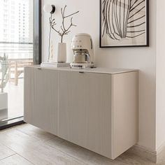 a kitchen area with a large white cabinet and art on the wall above it, along with a coffee maker