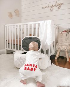 a baby sitting on the floor in front of a white crib