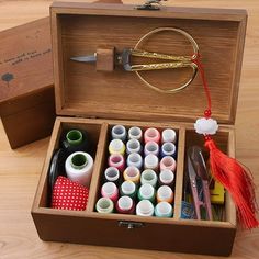 an open wooden box filled with lots of crafting supplies on top of a table