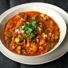 a white bowl filled with soup and garnished with herbs on a black surface