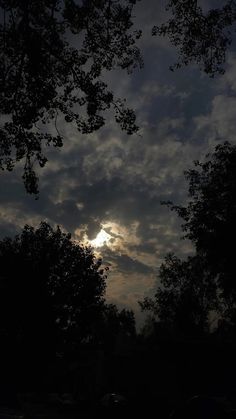 the sun is shining through the clouds in the dark sky above some trees and parked cars