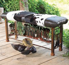 a bench with cowhides and cowboy boots on the ground next to it in front of some bushes