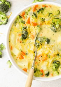 a white bowl filled with broccoli and carrots next to a wooden spoon