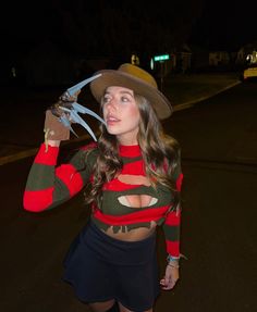 a woman wearing a hat and holding a pair of scissors in one hand while standing on the street