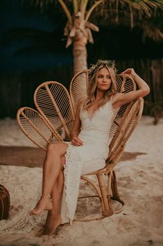 a woman in a white dress sitting on a wicker chair with palm trees behind her