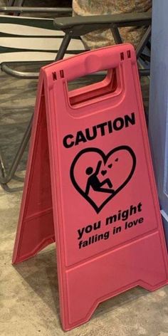 a pink caution sign sitting on the ground next to a blue box with a sticker that says caution you might falling in love