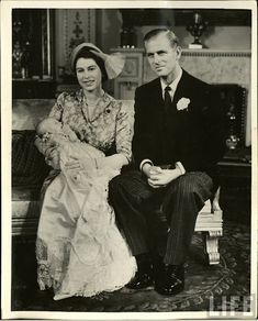 a black and white photo of a man and woman sitting on a couch holding a baby