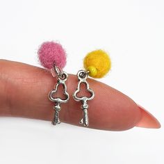 a person's hand holding two tiny keys and a pom - pom