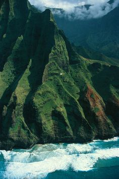 the mountains are covered in green grass and blue water with waves coming up from them