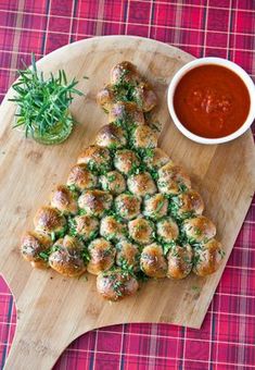 a christmas tree shaped pizza on a cutting board next to a bowl of tomato sauce