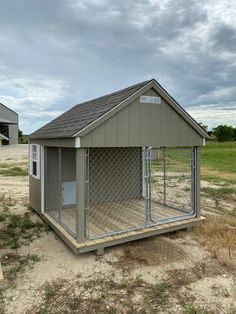 a small dog house with a fenced in area next to the grass and dirt