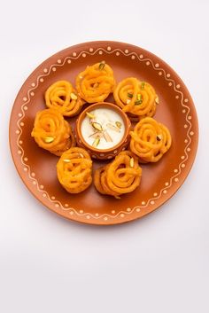 an orange plate topped with small food items on top of a white table next to a cup