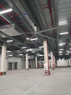 an empty parking garage with red piping on the ceiling and overhead lighting above it