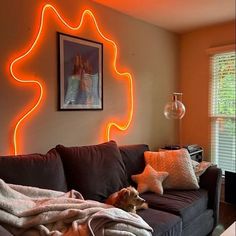 a dog laying on top of a brown couch under a neon light wall mounted above it