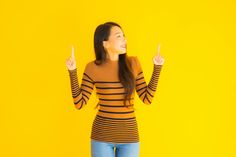 a woman standing in front of a yellow wall with her hands up and pointing to the side