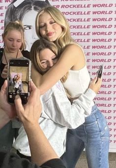 two women hugging each other while one takes a photo with her cell phone and another woman is taking a selfie