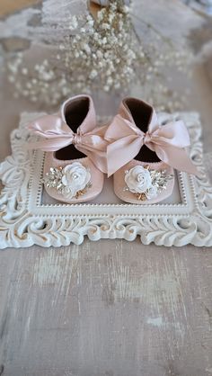 two pairs of baby shoes with pink bows on them sitting in a white frame next to flowers