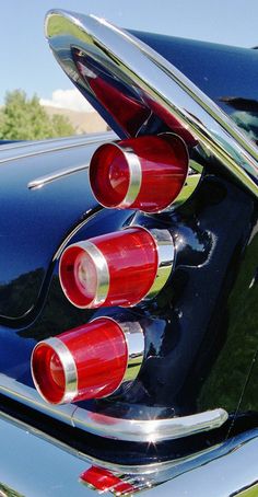 the rear end of a classic car with chrome trim and red tail lights on it