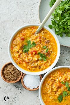 two bowls filled with soup next to spoons and parsley on the table top