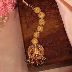 a necklace with gold coins and green beads on a wooden box next to pink flowers