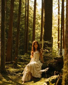 a woman is sitting in the woods wearing a dress