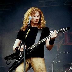 a man with long hair playing an electric guitar at a music festival in front of microphones