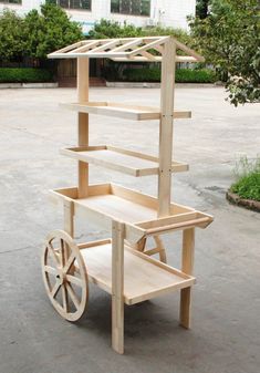 a cart made out of wood with wheels and shelves on the front, sitting in a parking lot